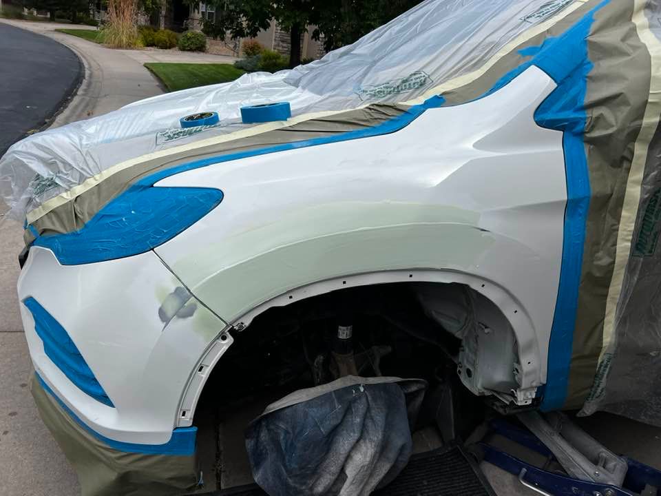 A white car is being painted with blue tape