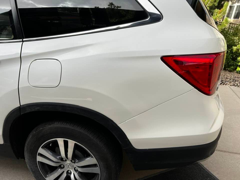 A white suv with a red tail light is parked on a sidewalk.