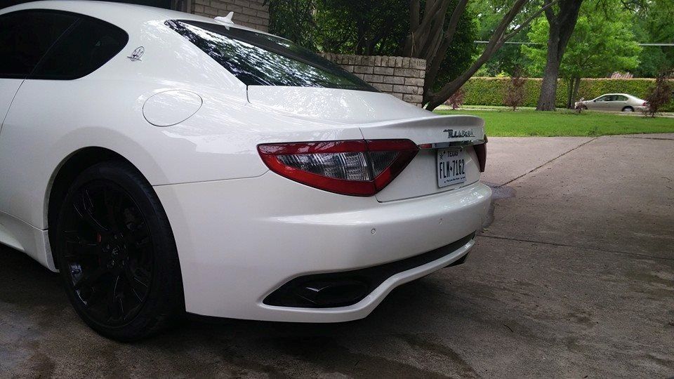 A white car is parked in a driveway with trees in the background.