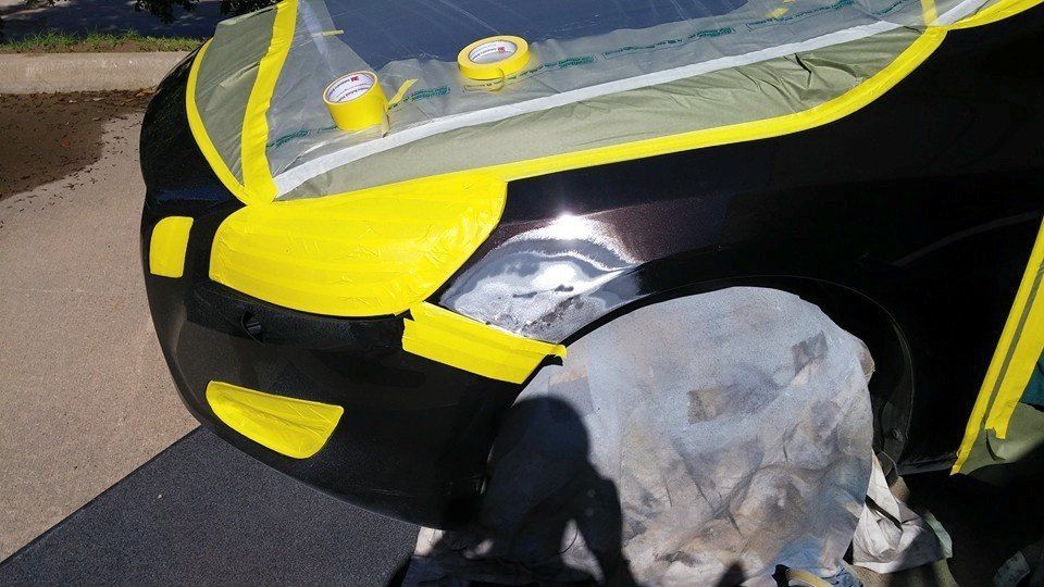 A black car with yellow tape on it is being painted