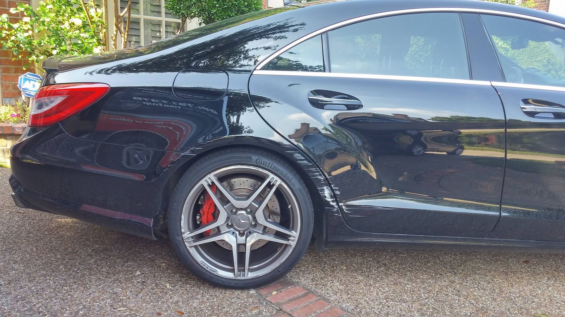 A black mercedes benz is parked on a gravel driveway.