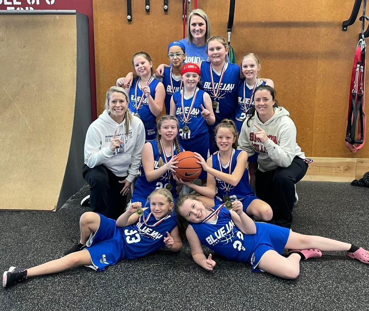 Youth basketball team posing with coaches indoors, holding a basketball and smiling on the court.