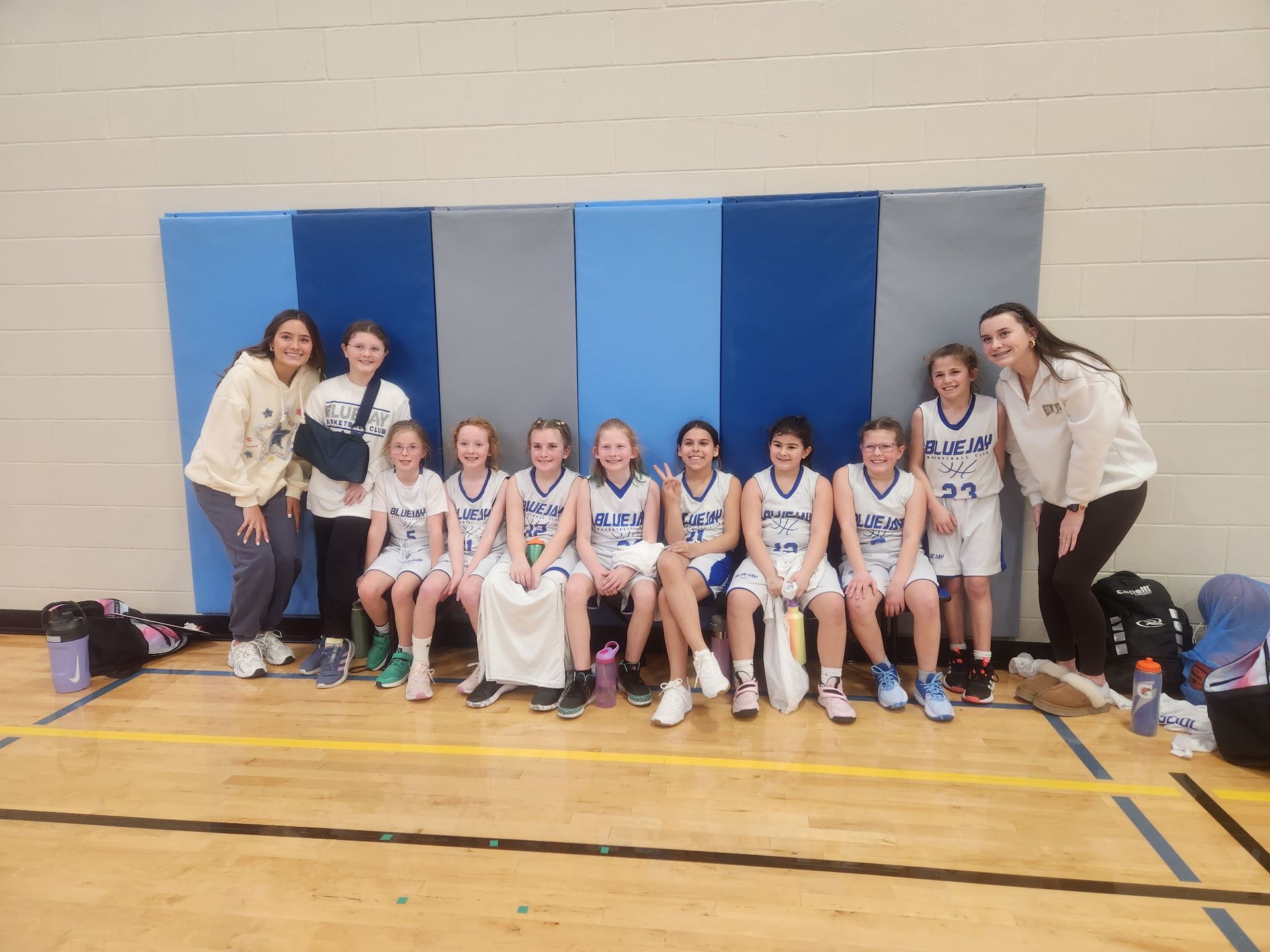 Basketball team group photo in a gym, posing in white and blue uniforms with coaches.