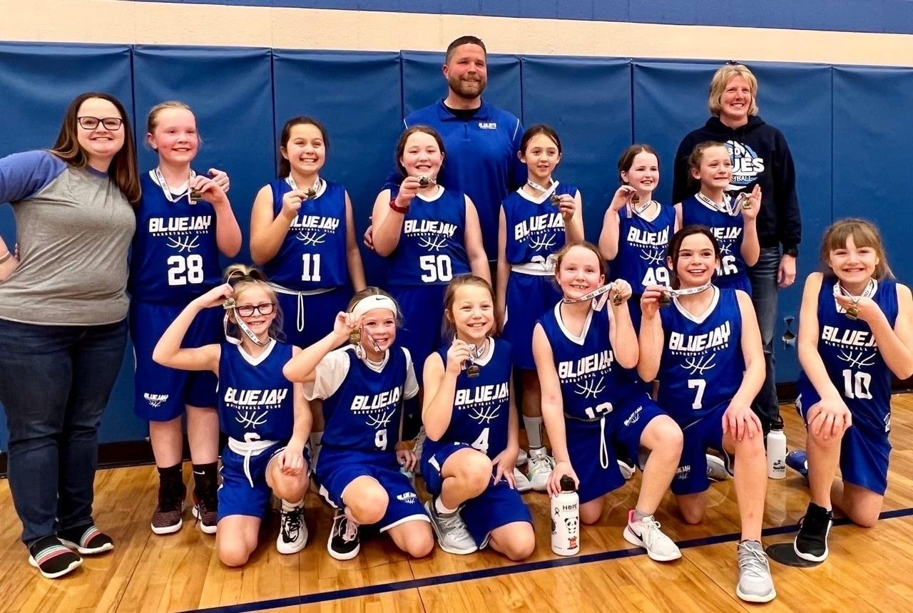 Youth basketball team and coaches posing in blue uniforms on an indoor gym court.