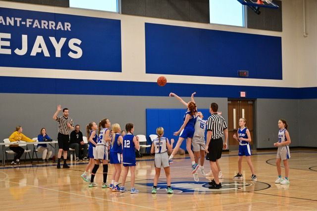 High school basketball tipoff in a gym, blue uniforms facing white uniforms under the hoop.