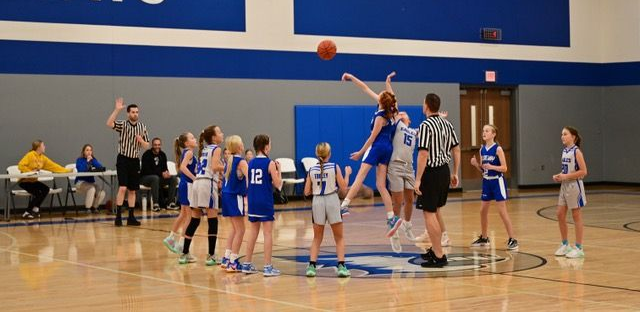 Youth basketball team posing with coaches indoors, holding a basketball and smiling on the court.