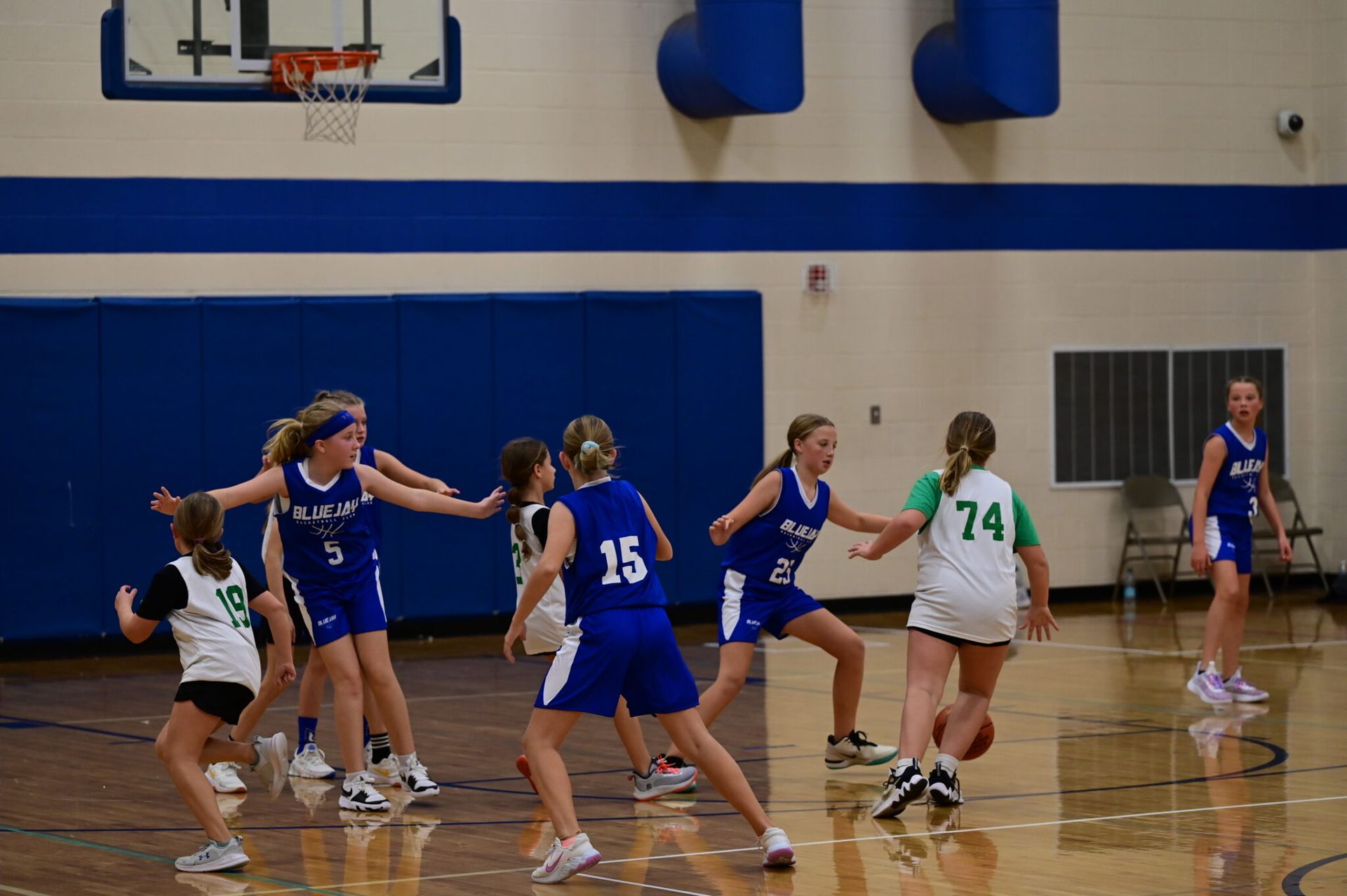 Girls playing basketball in a gym, with players in blue and white jerseys near the hoop