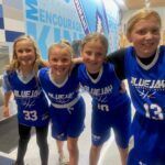 Four smiling Blue Jays youth athletes in blue uniforms posing indoors at a volleyball event