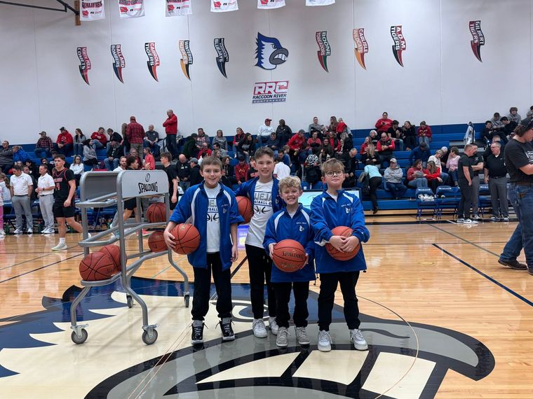 Youth basketball players pose with balls on a gym court during a school game.