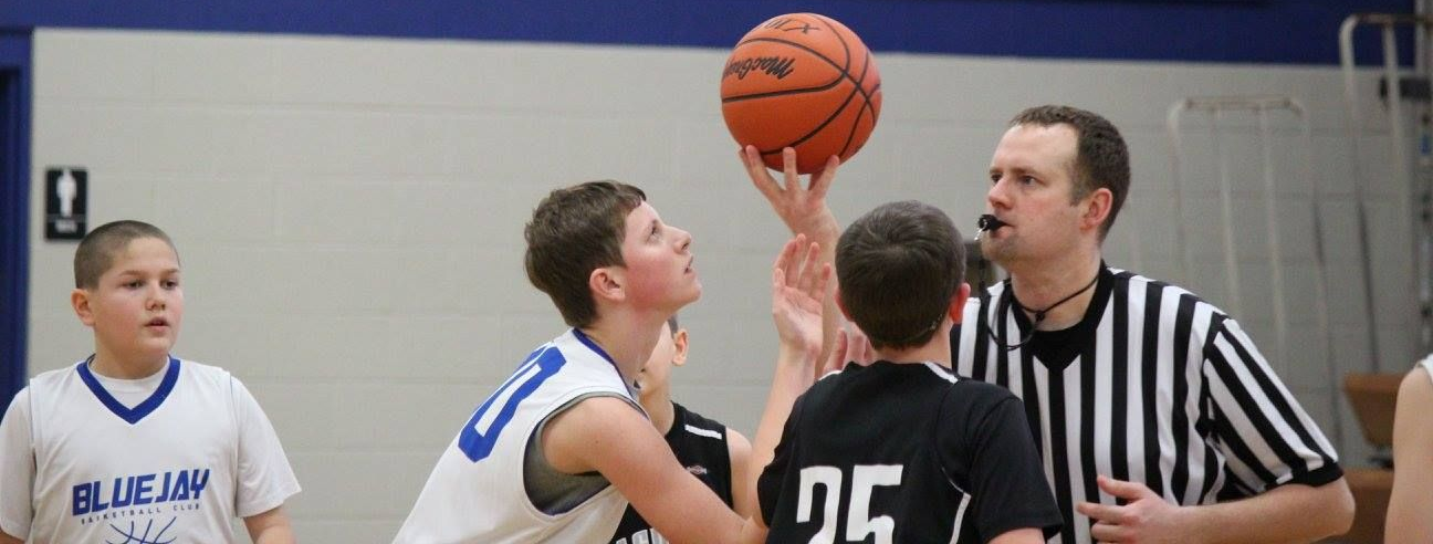 Youth basketball tip-off with players and referee under the hoop.