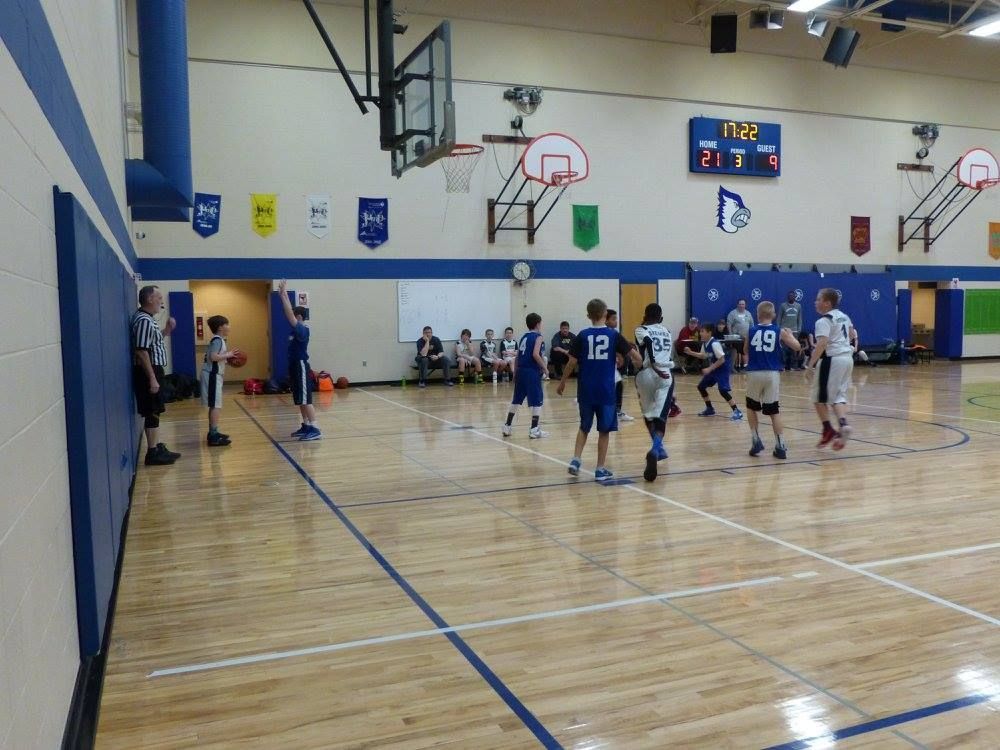Basketball game in a gym, with players competing near the hoop and spectators seated along the wall.