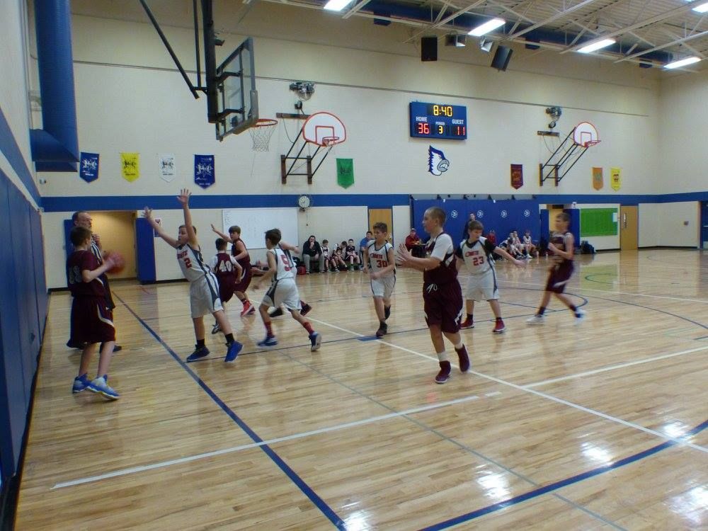 Three kids in team basketball uniforms posing indoors, one holding a basketball