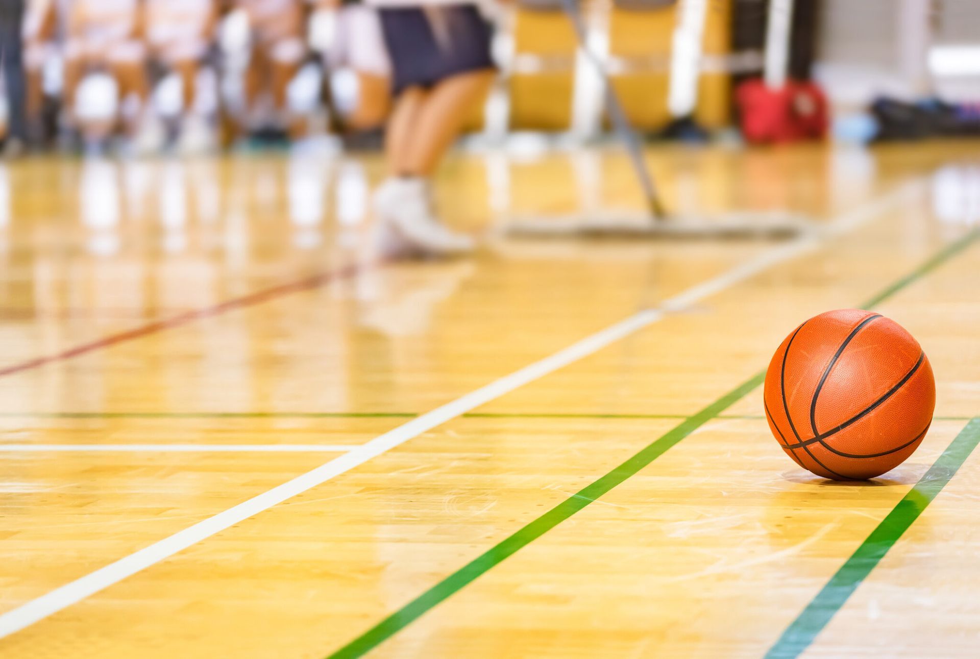 Orange basketball on a gym floor with blurred players in the background