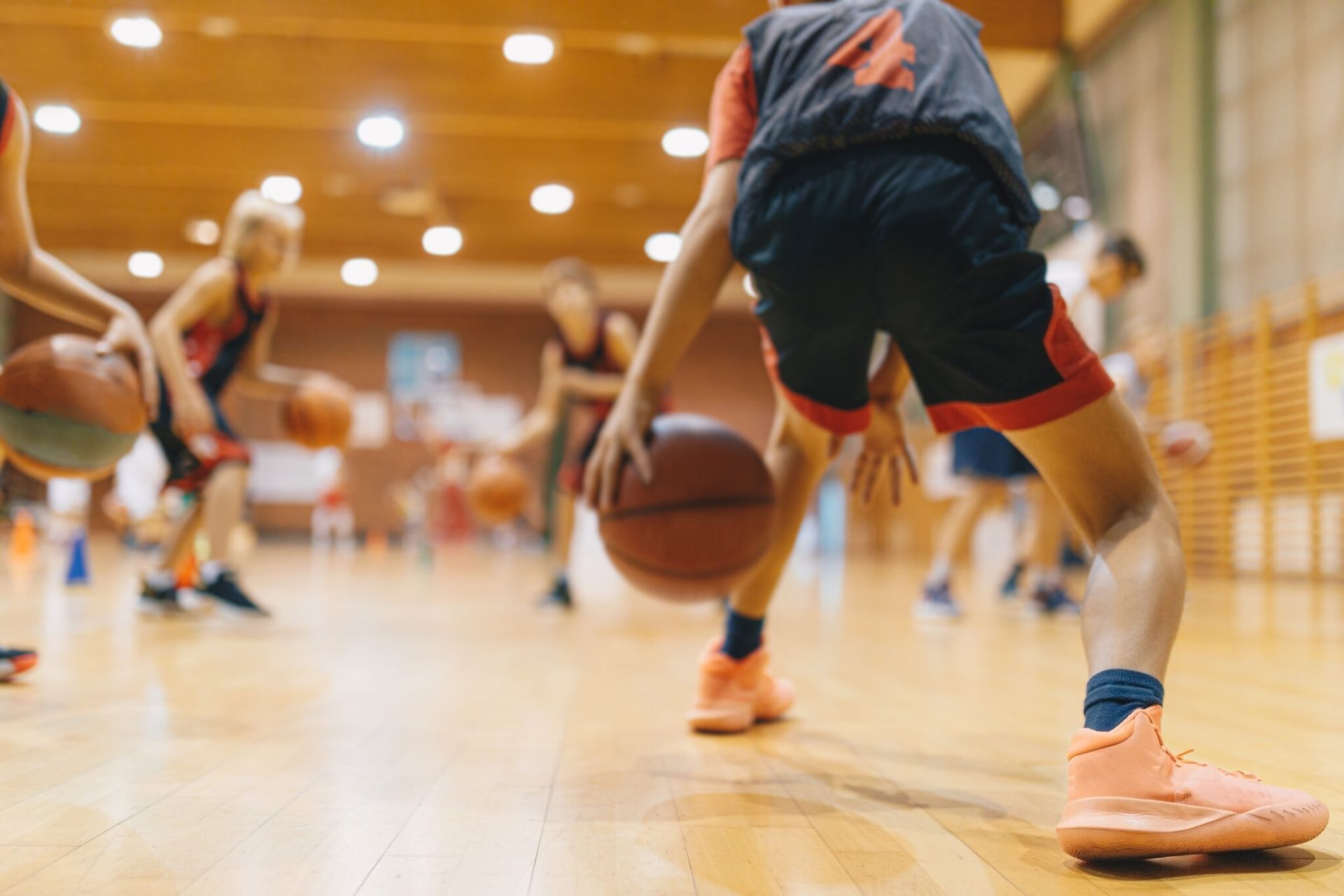 Youth basketball practice in a gym, with players dribbling orange balls on a polished court.