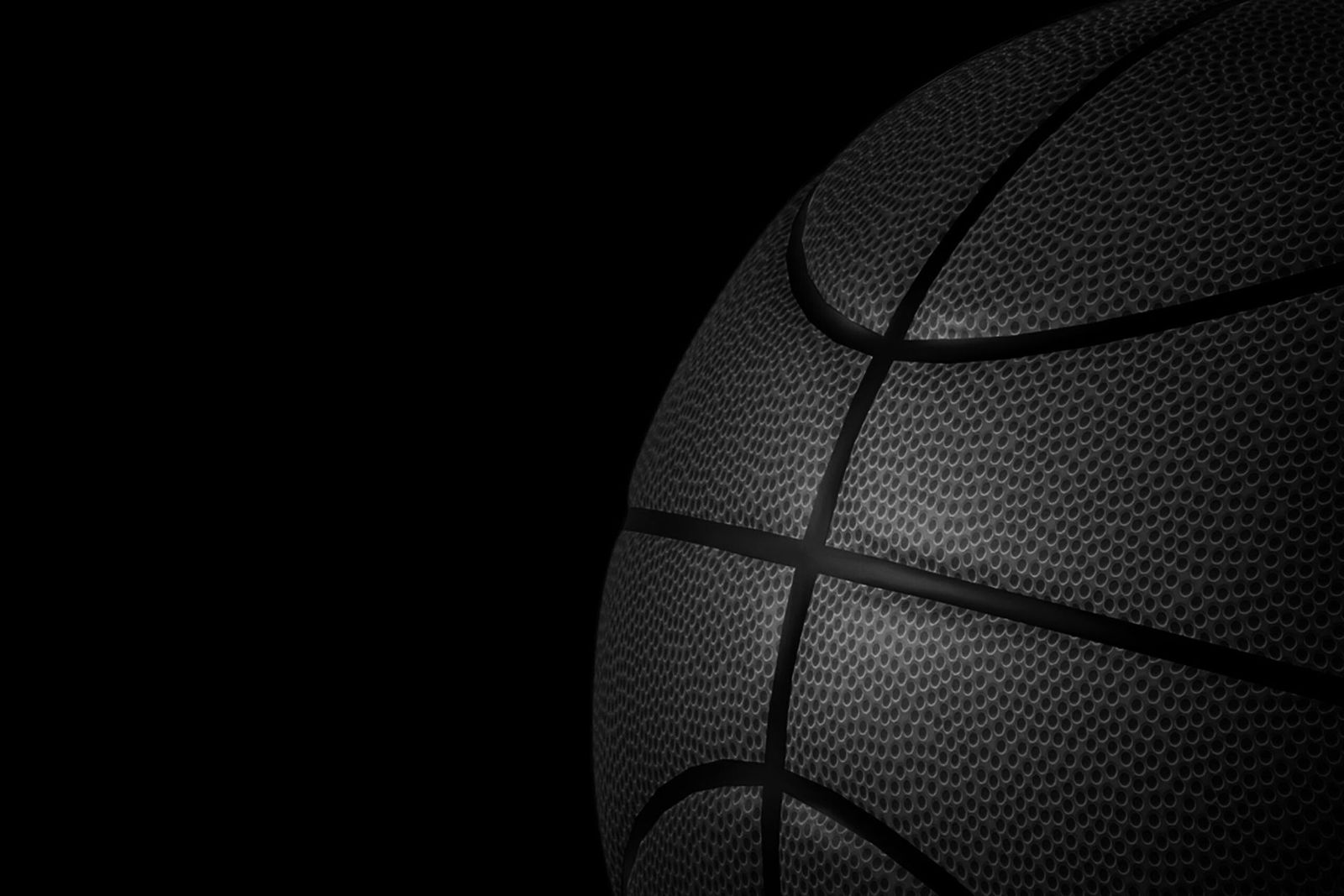 Close-up of a black basketball on a dark background, showing textured surface and curved seams