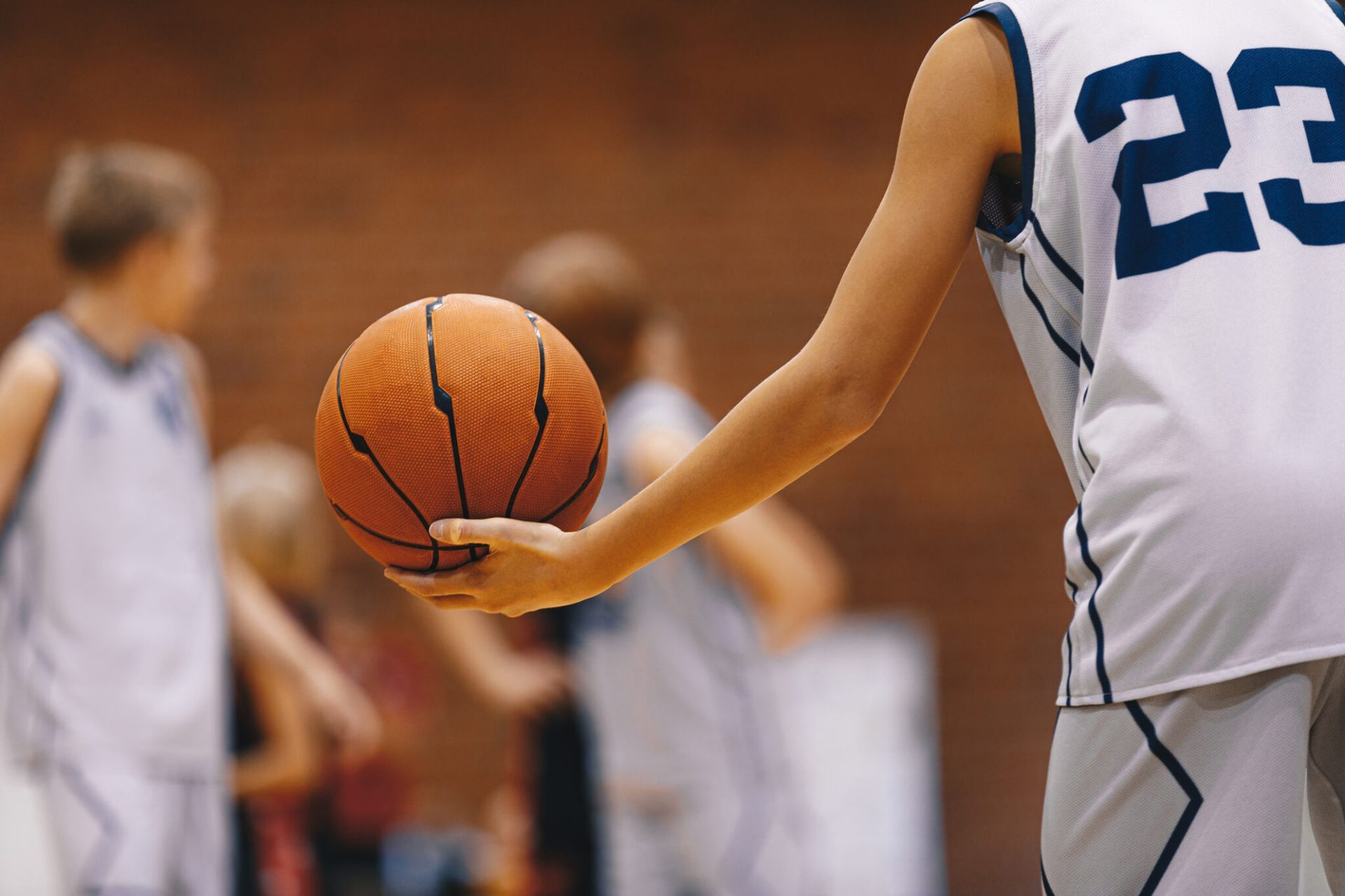 Basketball player dribbling orange ball on indoor court, with teammates blurred in background