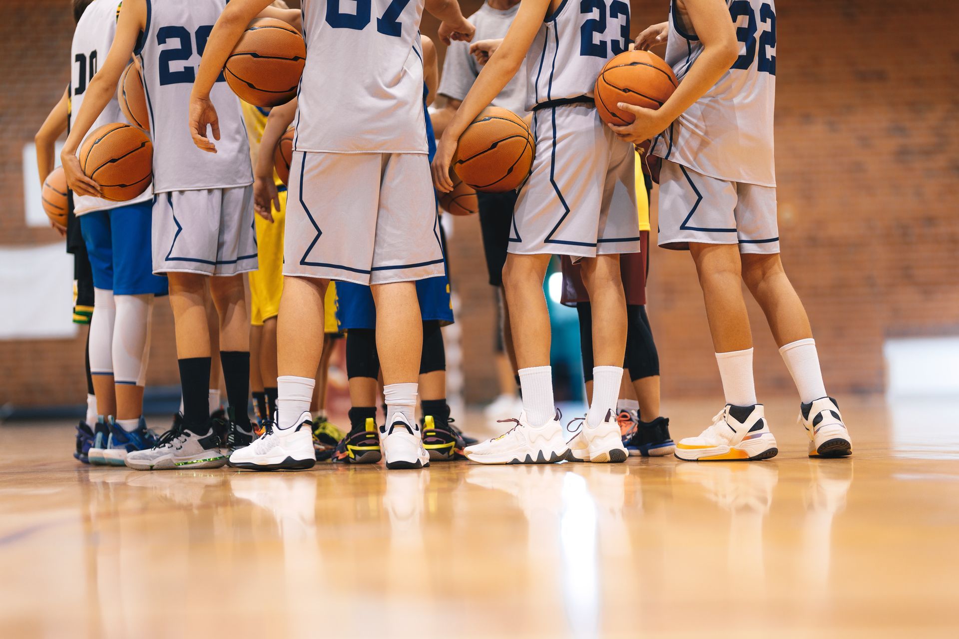 Basketball players huddled on a gym court, holding orange basketballs and wearing white and blue uniforms.