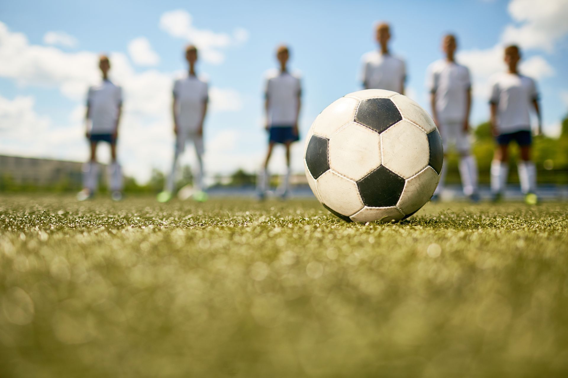 Soccer ball on grass with players blurred in the background on a sunny field