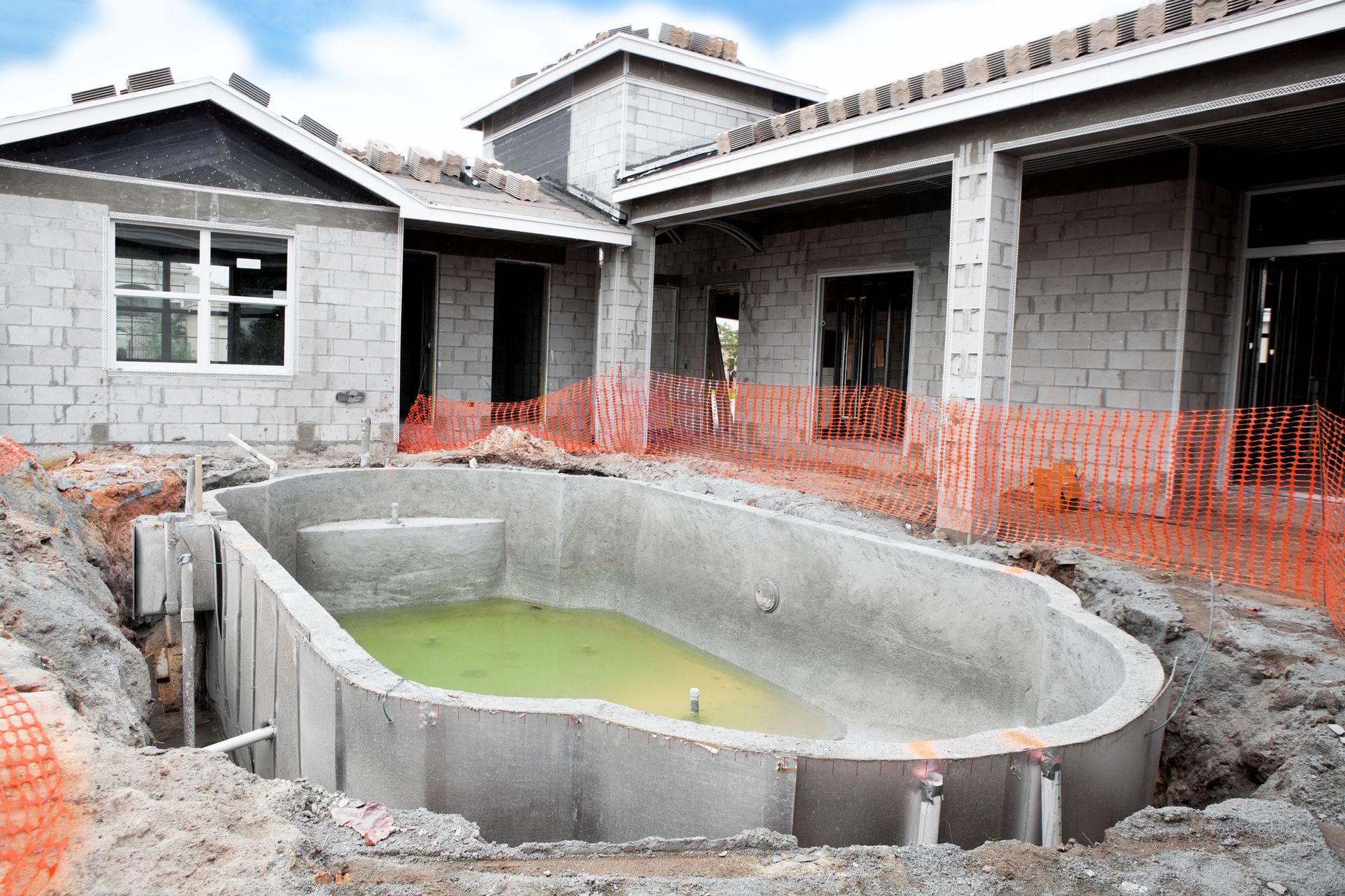 A swimming pool is being built in front of a house under construction.
