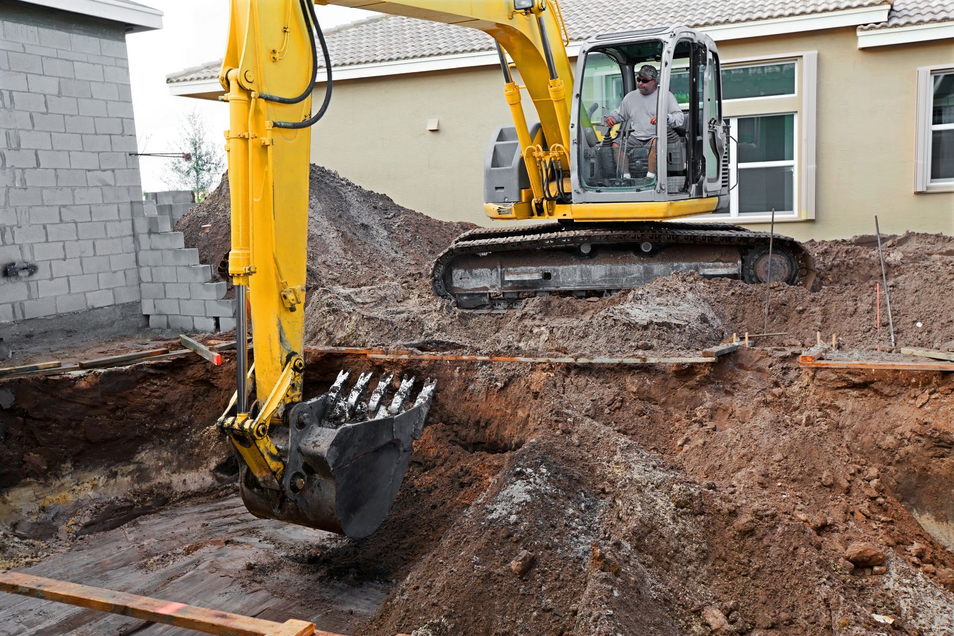A yellow excavator is digging a hole in front of a house.