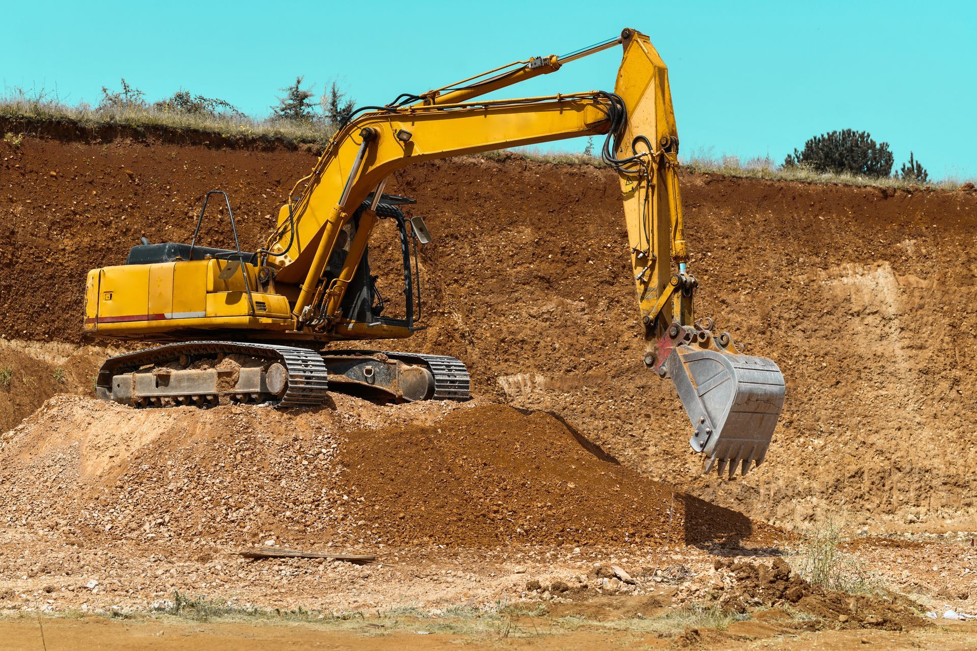A yellow excavator is digging a hole in a dirt field.
