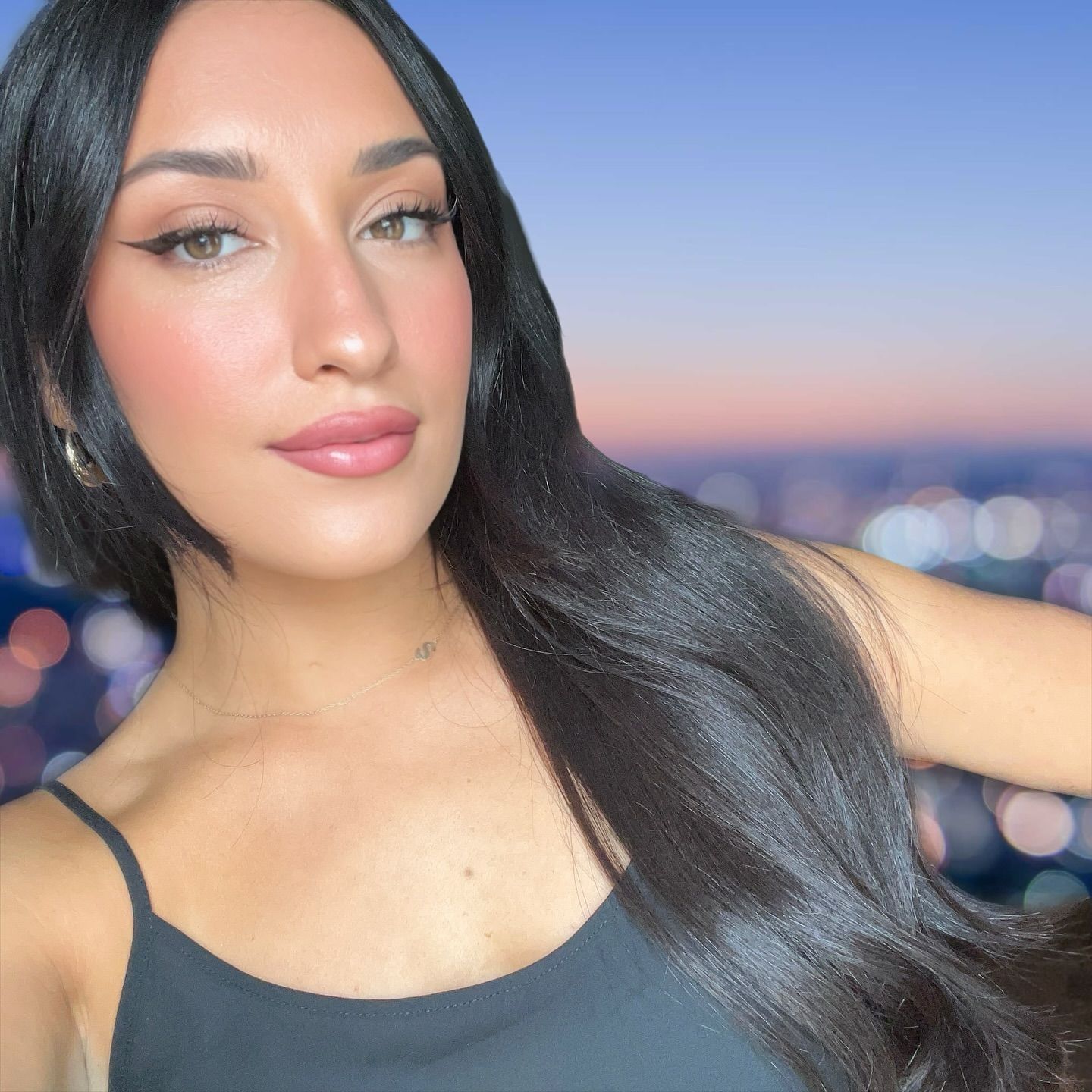 A woman with long black hair is wearing a black tank top