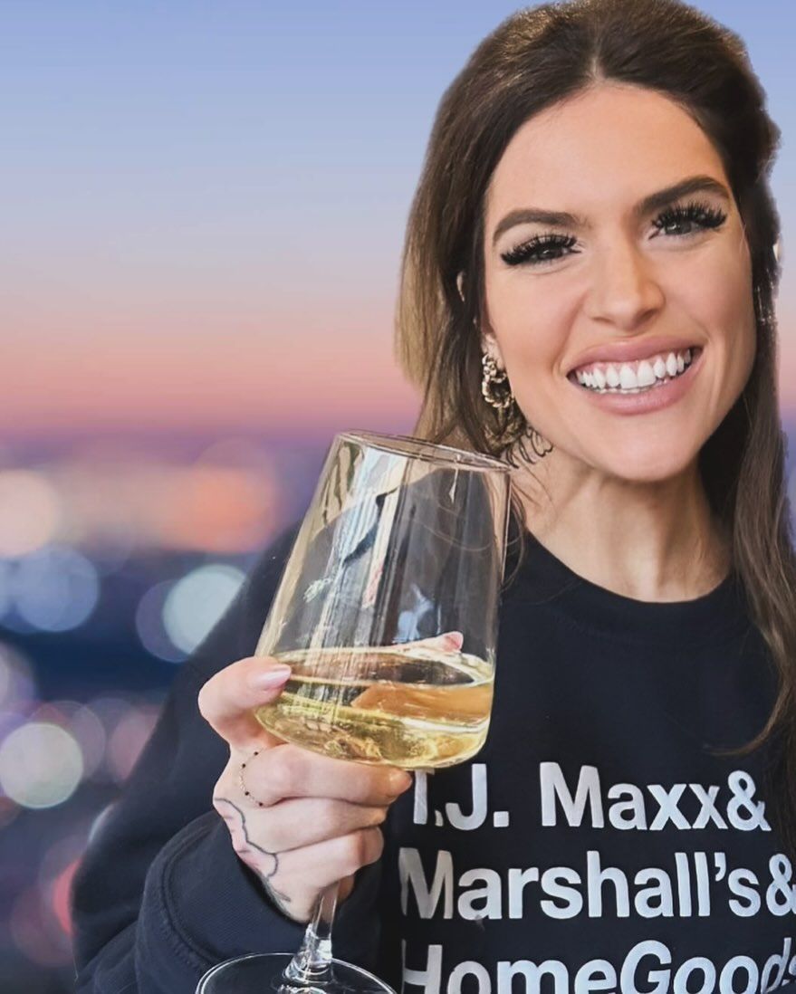 A woman holding a glass of wine wearing a shirt that says t.j. maxx & marshall 's & homegood