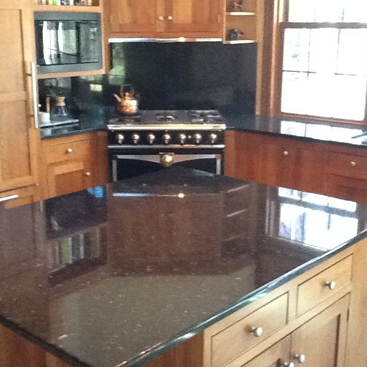 Modern kitchen with black granite island, wooden cabinets, and a stainless-steel stove near a window.