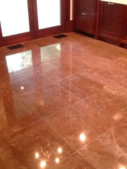 Polished brown marble floor reflecting light in an empty room with wood-paneled walls and glass doors