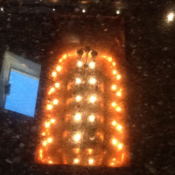 Glowing orange arched light display in a dark indoor setting, with reflections on a glass surface