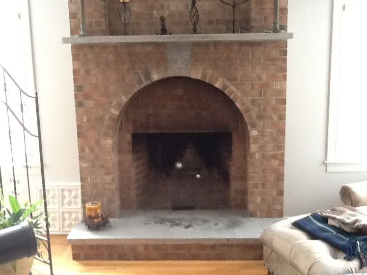 Brick fireplace with a dark arched opening in a living room, flanked by windows and a couch.