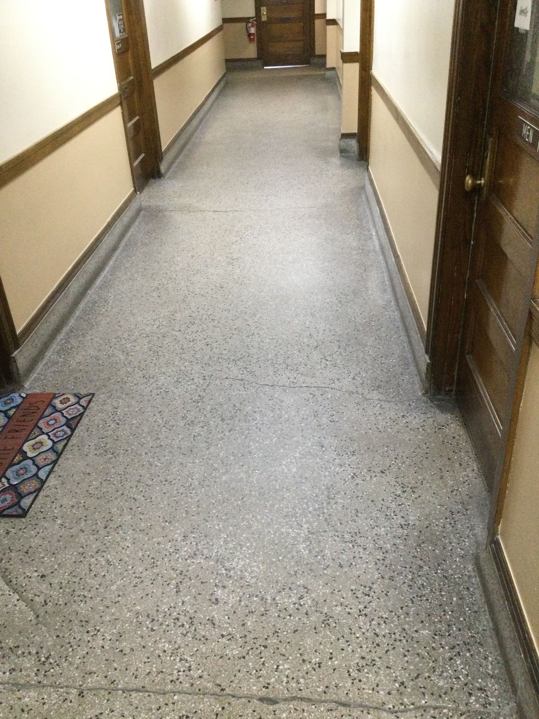 Empty indoor hallway with beige walls, wood trim, and speckled gray floor tile.
