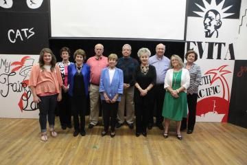 Group of eight people standing on a stage in front of a CATV banner and red-and-white wall art
