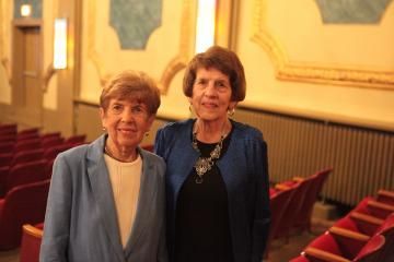 Two people standing in a warmly lit auditorium with red seats