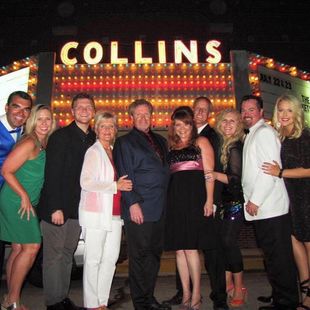 Group of people posing in front of the illuminated Collins sign at night.