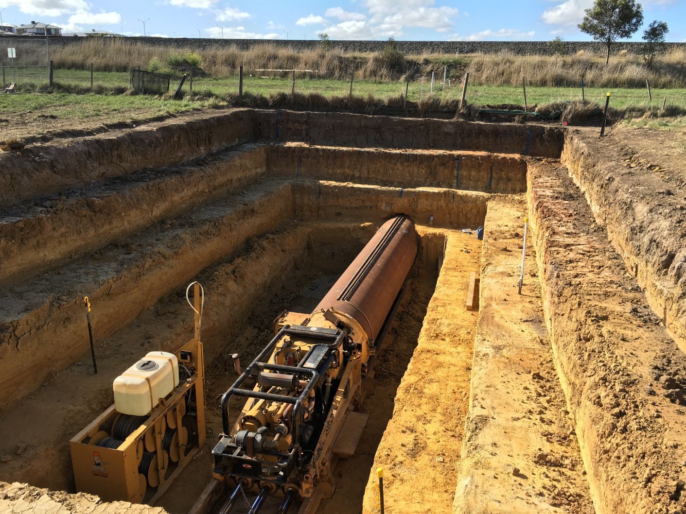 A large pipe is being drilled into the ground in a trench.