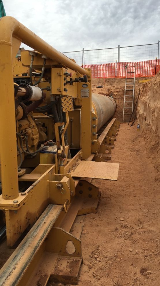 A yellow machine is sitting in the dirt next to a ladder.
