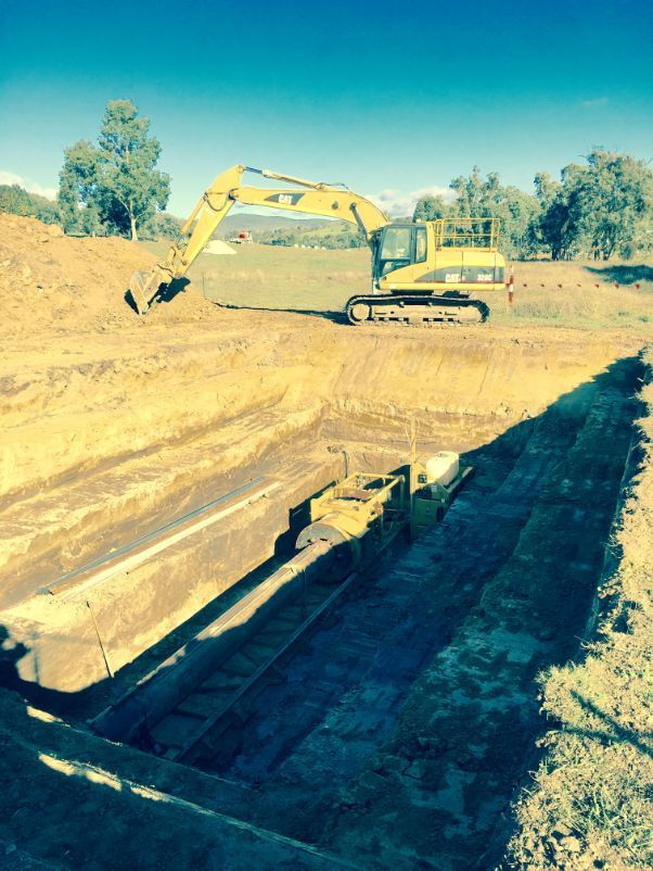 A yellow excavator is digging a trench in a field.