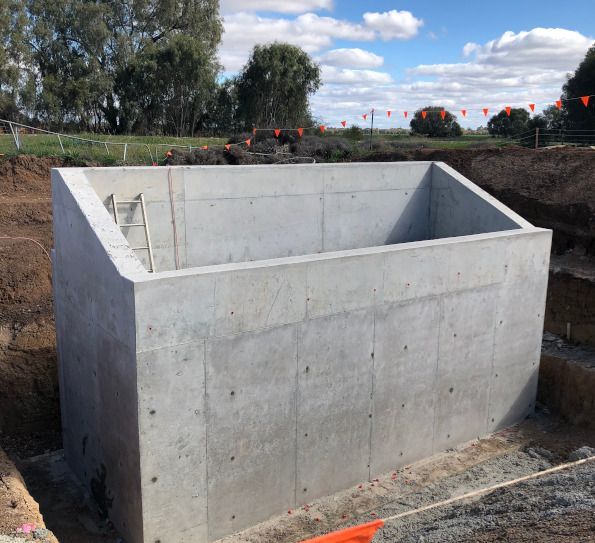A large concrete block with a ladder attached to it is sitting in the middle of a dirt field.