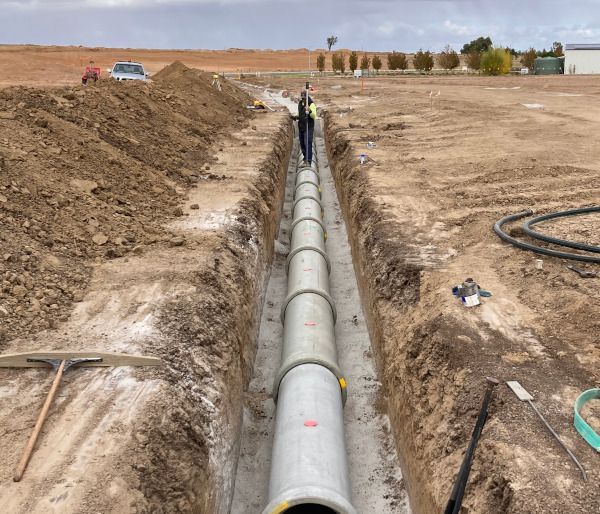 A man is standing in a trench next to a large pipe.