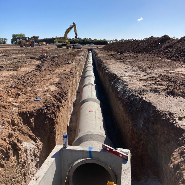 A large concrete pipe is being installed in a trench