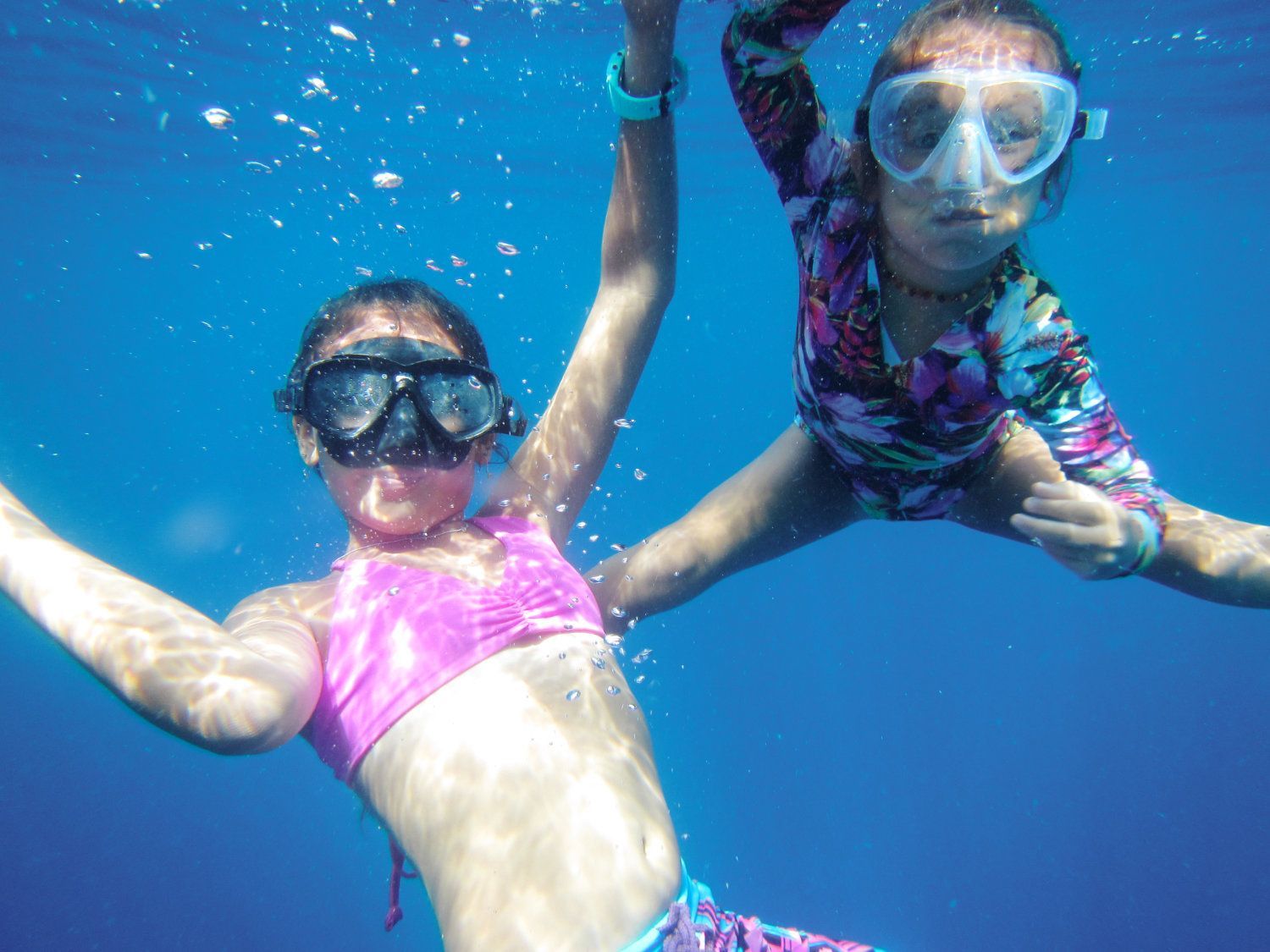 Two people snorkeling underwater, arms raised. 