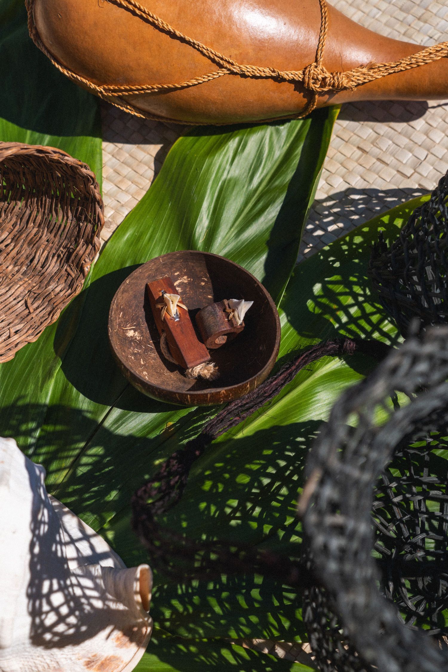 Coconut bowl with wood, on a large green leaf, surrounded by woven objects and a gourd.