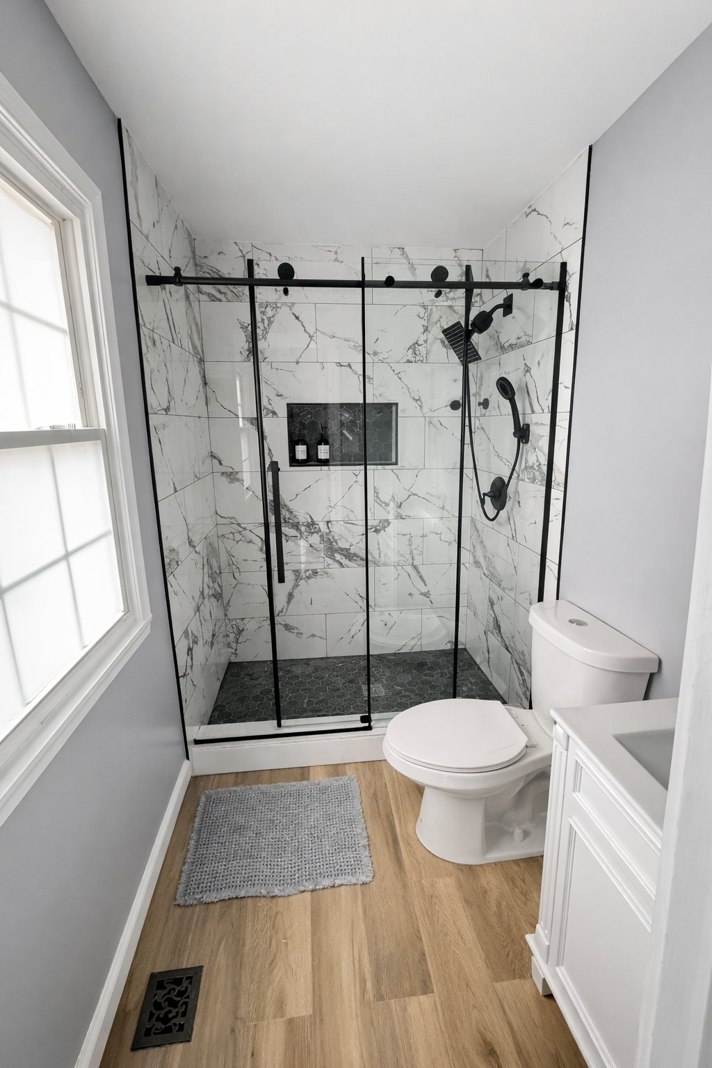Professional bathroom remodel in Clarksville MD featuring white marble tile shower with black sliding glass door, matte black hardware, and hex mosaic floor by Handyman on Demand