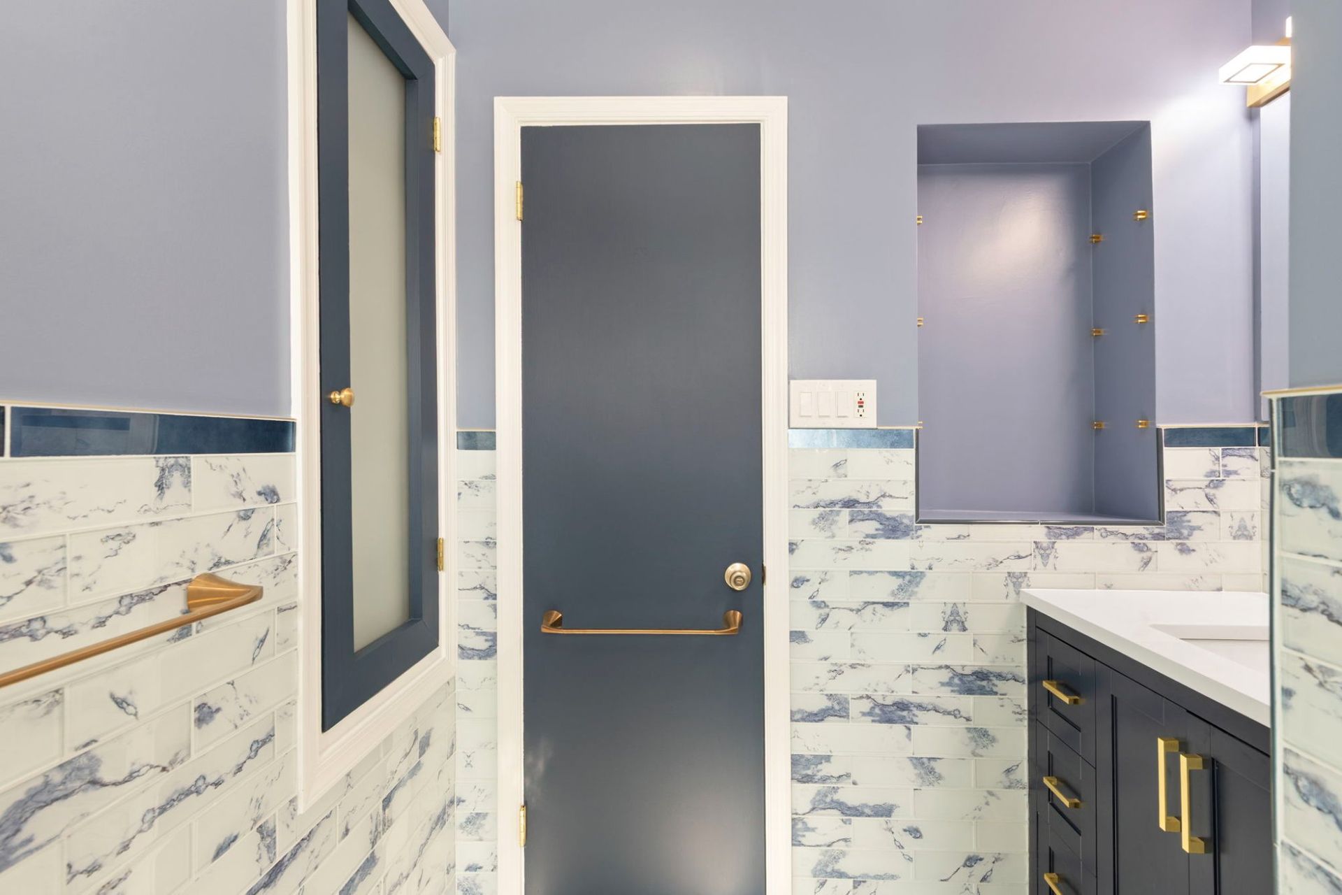 Bathroom remodel with navy accent door, built-in shower niche, and marble tile surround by professional contractor Handyman on Demand serving Clarksville MD