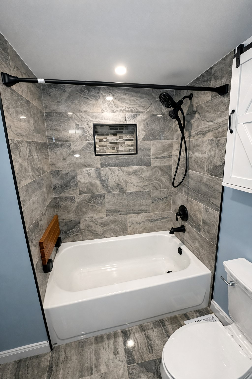 Local bathroom remodel in Clarksville MD with tub and shower surround, gray stone tile, matte black fixtures, barn door wall cabinet, and recessed niche by Handyman on Demand