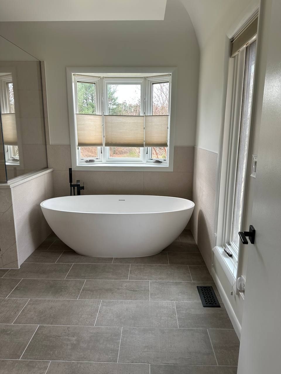 Professional bathroom remodeling and renovation in Clarksville MD with freestanding soaking tub, large format gray floor tile, and neutral wall tile by Handyman on Demand