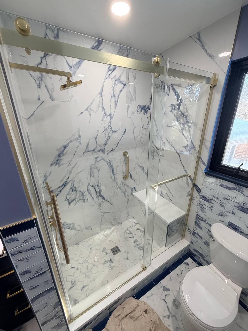 Custom bathroom renovation in Clarksville MD with blue marble tile walk-in shower, brushed gold sliding glass door, hex floor tile, and navy blue vanity by Handyman on Demand