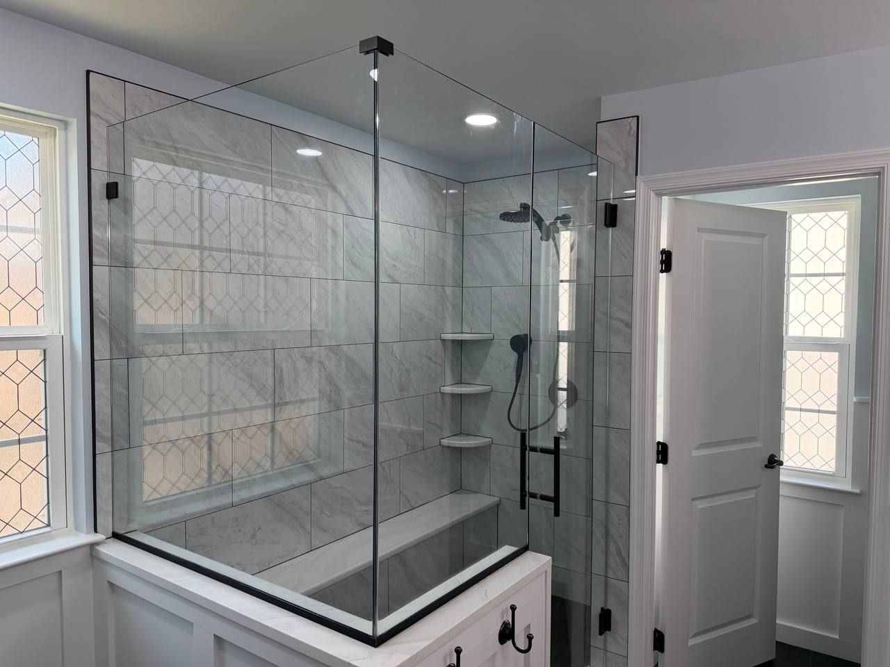 Custom shower remodel and bathroom renovation in Clarksville MD with white marble tile surround, frameless glass enclosure, built-in bench seat, and matte black hardware by Handyman on Demand