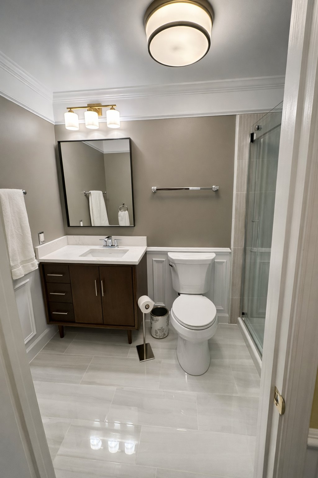 Full bathroom renovation and remodel in Clarksville MD with dark walnut vanity, white wainscoting, glass shower enclosure, crown molding, and polished large format tile floor by Handyman on Demand